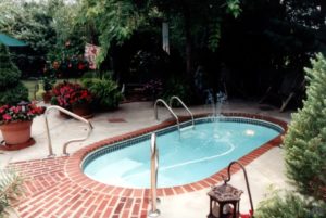 Inground swimming pool with brick surround and shady trees